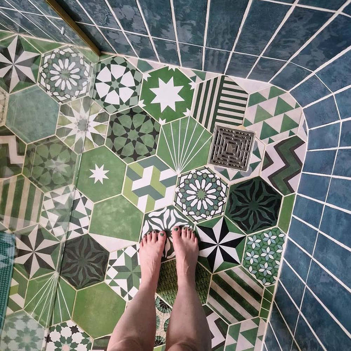 Bathroom featuring Fayrouz Verde Hexagon Patchwork Moroccan-style porcelain tiles in an 18.7×21.6cm hexagon format, combining intricate geometric and star patterns in layered green, sage and charcoal tones, paired with deep blue glazed wall tiles, brushed brass fixtures and a curved walk-in shower for a bold, character-led finish.