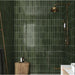 Bathroom shower area featuring Zellige Botanical Green Brick 6.5 × 20cm Moroccan-style ceramic wall tiles in deep botanical green tones, laid in a vertical brick layout, paired with vintage-style brass shower fittings and natural wood accents for a rich, atmospheric zellige-effect finish.