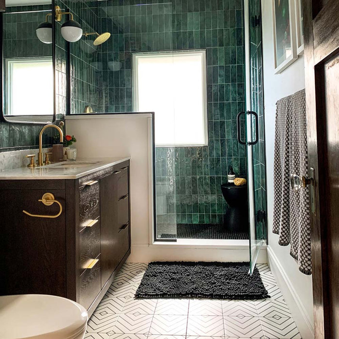 Bathroom featuring Zellige Royal Green Brick 6.5 × 20cm Moroccan-style ceramic wall tiles in rich deep green tones, installed in a vertical brick layout within a walk-in shower, paired with brass fittings, dark cabinetry and patterned floor tiles for a striking zellige-effect finish.