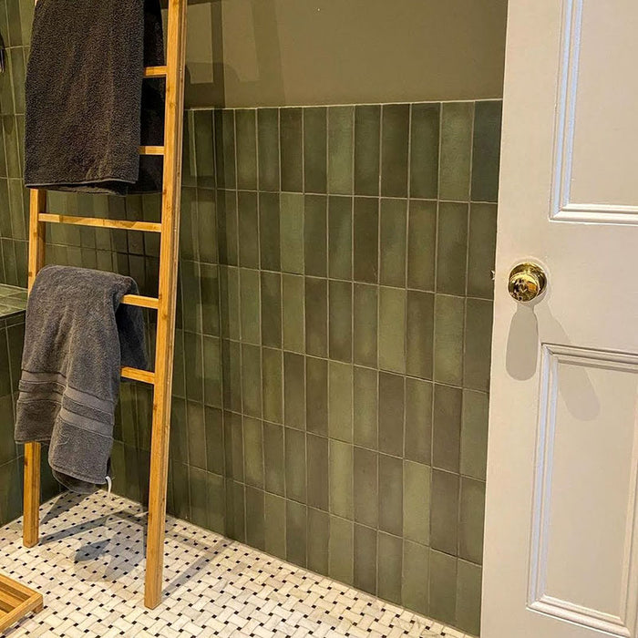 Bathroom featuring Zellige Malachite Green 6.5×20cm Moroccan-style ceramic brick tiles, installed on the walls around a bath and shower, paired with brushed brass fittings, a wooden vanity unit and a stone basin for a warm, spa-like finish.