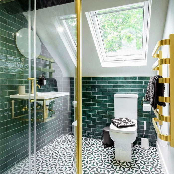 Bathroom featuring Zellige Royal Green Brick 6.5 × 20cm Moroccan-style ceramic wall tiles in rich deep green tones, laid in a horizontal brick layout around a wall-mounted basin, paired with brass fittings, a glass shower screen and patterned floor tiles for a bold, elegant zellige-effect finish.