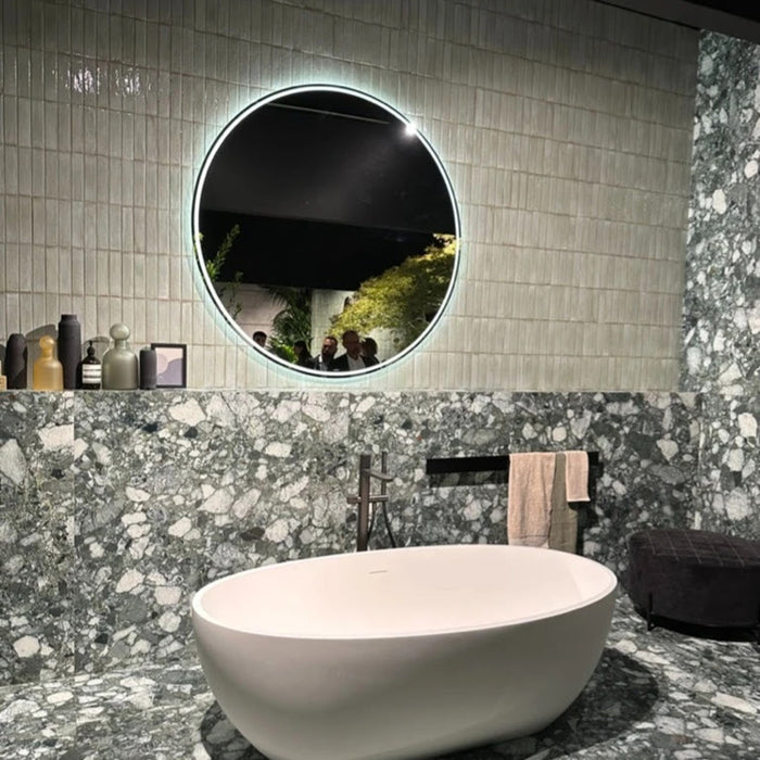 Puzzle Breeze Green Brick Rectified 5x20cm porcelain tiles used as a vertical bathroom wall feature, showcasing soft breeze green tones with subtle speckling and gentle shade variation. The slim brick format adds texture and height, beautifully contrasting with bold terrazzo-style surfaces and a contemporary freestanding bath for a striking, design-led finish.