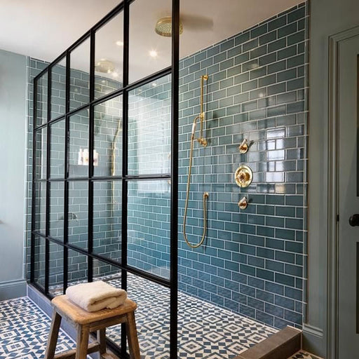 Walk-in shower featuring Pimlico River Blue 7.5x15cm crackle glaze metro tiles in glossy blue tones, styled in a brick layout with brass fittings and black framed screen for a bold bathroom wall tile statement.