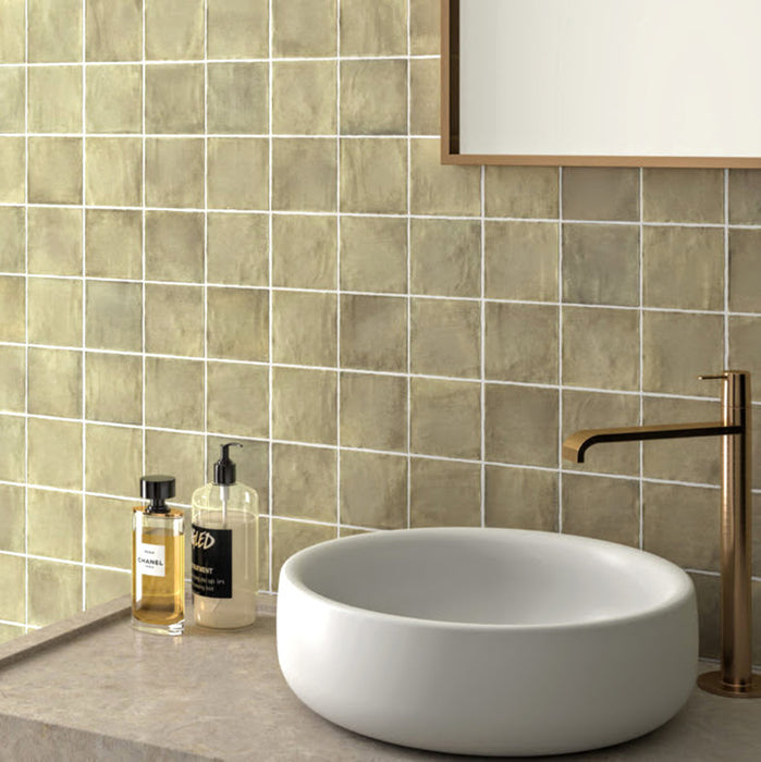 Bathroom featuring Zellige Weald Green 10×10cm Moroccan-style ceramic square tiles installed on the walls behind a vanity, showcasing soft green tonal variation and a handmade-look glazed finish, paired with a stone countertop, round basin and brass tapware.