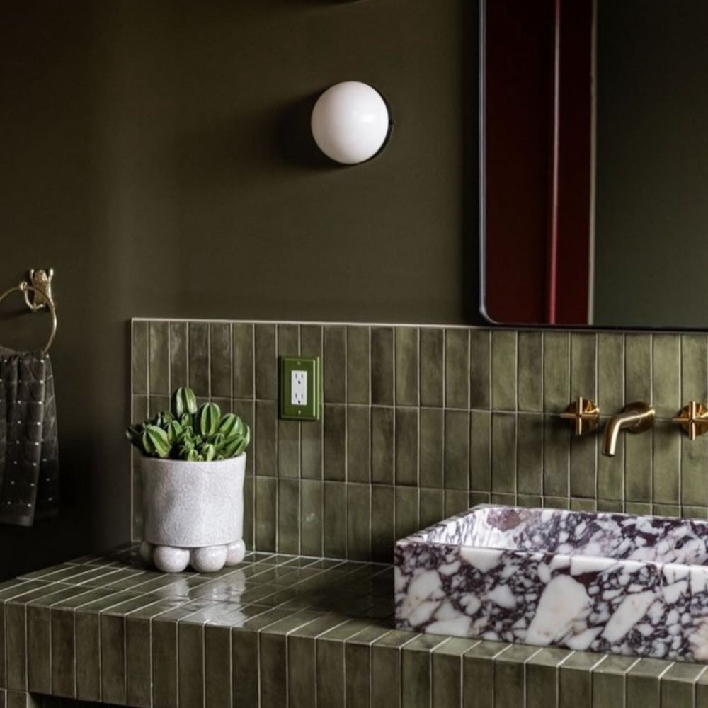 Benomar Verde Moroccan mini brick gloss tiles in 5x15cm format used on bathroom walls and vanity surround, featuring rich green tones with subtle shade variation, styled with brass fittings and a marble basin for a bold, design-led statement.