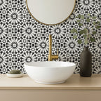 Fez Winter Moroccan-style porcelain tiles used as a striking bathroom splashback, featuring an intricate black and white geometric pattern inspired by traditional Moroccan design. The 20 × 20cm tiles create a bold, high-contrast backdrop, paired here with a white countertop basin, brushed brass tapware and soft neutral accessories to balance the graphic pattern and give the space a clean, contemporary finish.