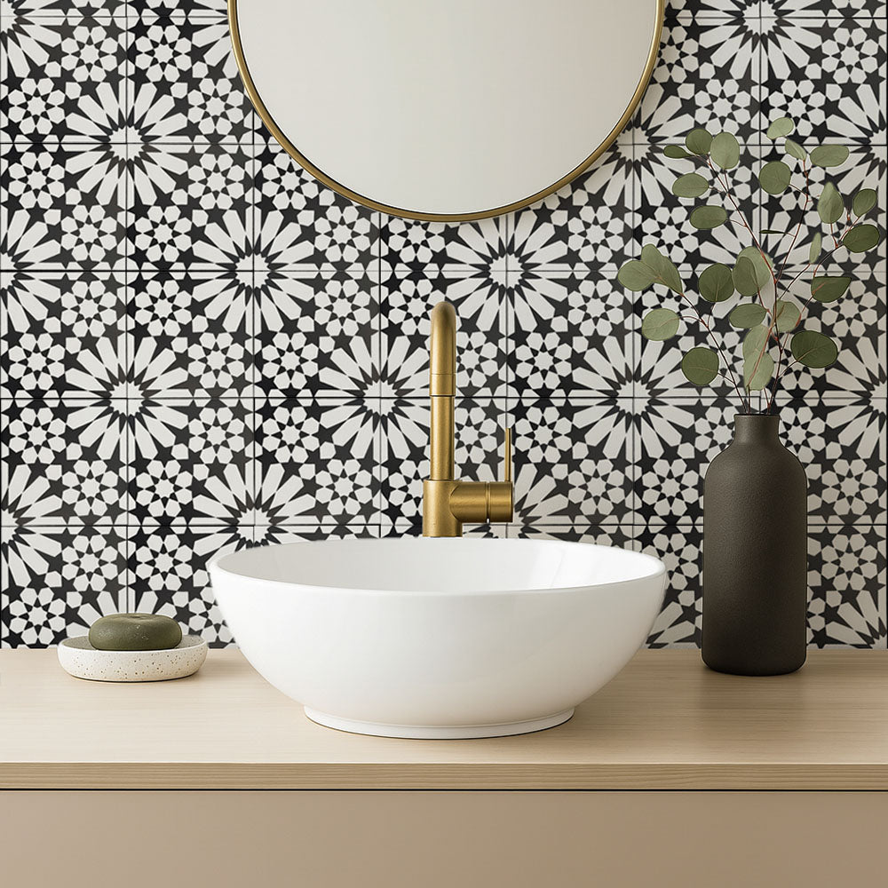 Fez Winter Moroccan-style porcelain tiles used as a striking bathroom splashback, featuring an intricate black and white geometric pattern inspired by traditional Moroccan design. The 20 × 20cm tiles create a bold, high-contrast backdrop, paired here with a white countertop basin, brushed brass tapware and soft neutral accessories to balance the graphic pattern and give the space a clean, contemporary finish.