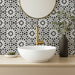 Fez Winter Moroccan-style porcelain tiles used as a striking bathroom splashback, featuring an intricate black and white geometric pattern inspired by traditional Moroccan design. The 20 × 20cm tiles create a bold, high-contrast backdrop, paired here with a white countertop basin, brushed brass tapware and soft neutral accessories to balance the graphic pattern and give the space a clean, contemporary finish.