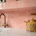 Kitchen featuring Benomar Pink Gloss 5x15cm Moroccan-style wall tiles in a geometric layout, styled with pastel blue cabinetry, brass fixtures, and decorative accents for a playful contemporary interior.