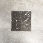 Four Fayrouz Black 15.2x15.2cm natural marble tiles with a honed finish arranged together, showcasing deep black tones, bold white veining and natural variation against a neutral textured background.