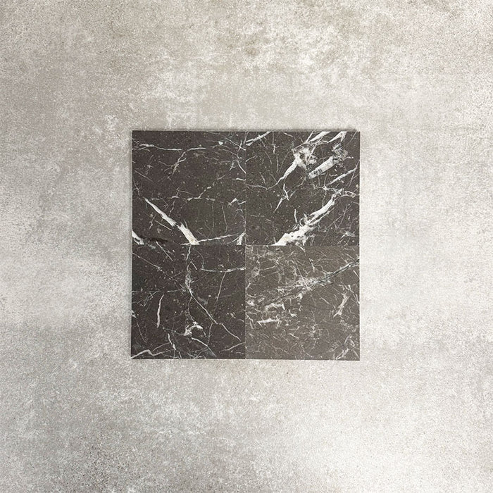 Four Fayrouz Black 15.2x15.2cm natural marble tiles with a honed finish arranged together, showcasing deep black tones, bold white veining and natural variation against a neutral textured background.
