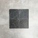 Four Fayrouz Black 15.2x15.2cm natural marble tiles with a tumbled finish arranged together, showcasing deep charcoal tones, natural veining and surface variation against a neutral textured background.