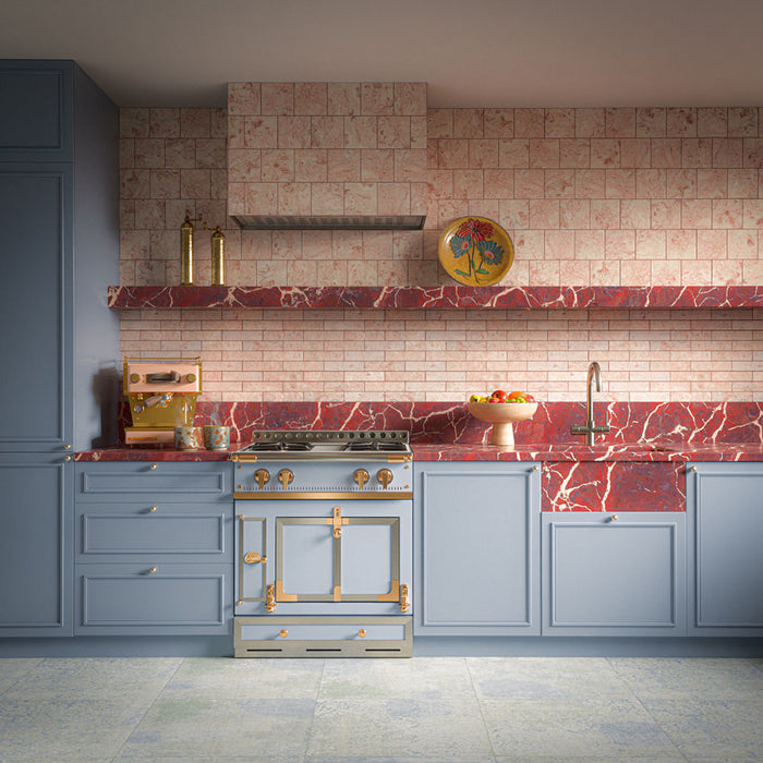 Kitchen featuring Boho Ocean Blue Patterned 59.55cm x 59.55cm floor tiles, paired with pale blue shaker cabinetry, red marble worktops, blush pink natural marble splashback tiles, brass fittings and a traditional range cooker.
