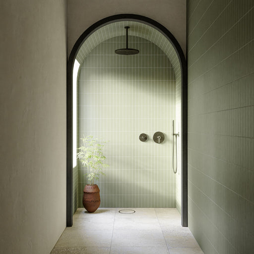 Walk-in shower featuring Boho Ocean Sahara Patterned 59.55cm x 59.55cm floor tiles, paired with vertically laid sage green wall tiles, an arched entrance, brushed metal fittings and natural décor.