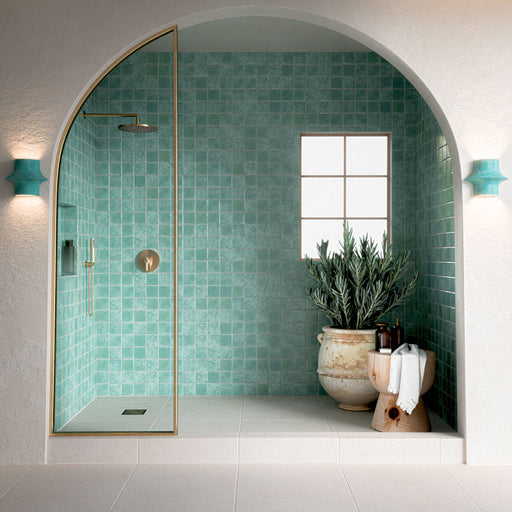 Contemporary walk-in shower featuring Bora Bora Aqua Square 10cm x 10cm flux glaze wall tiles, paired with white floor tiles, brass shower fittings and an arched alcove for a bright Mediterranean-inspired bathroom.