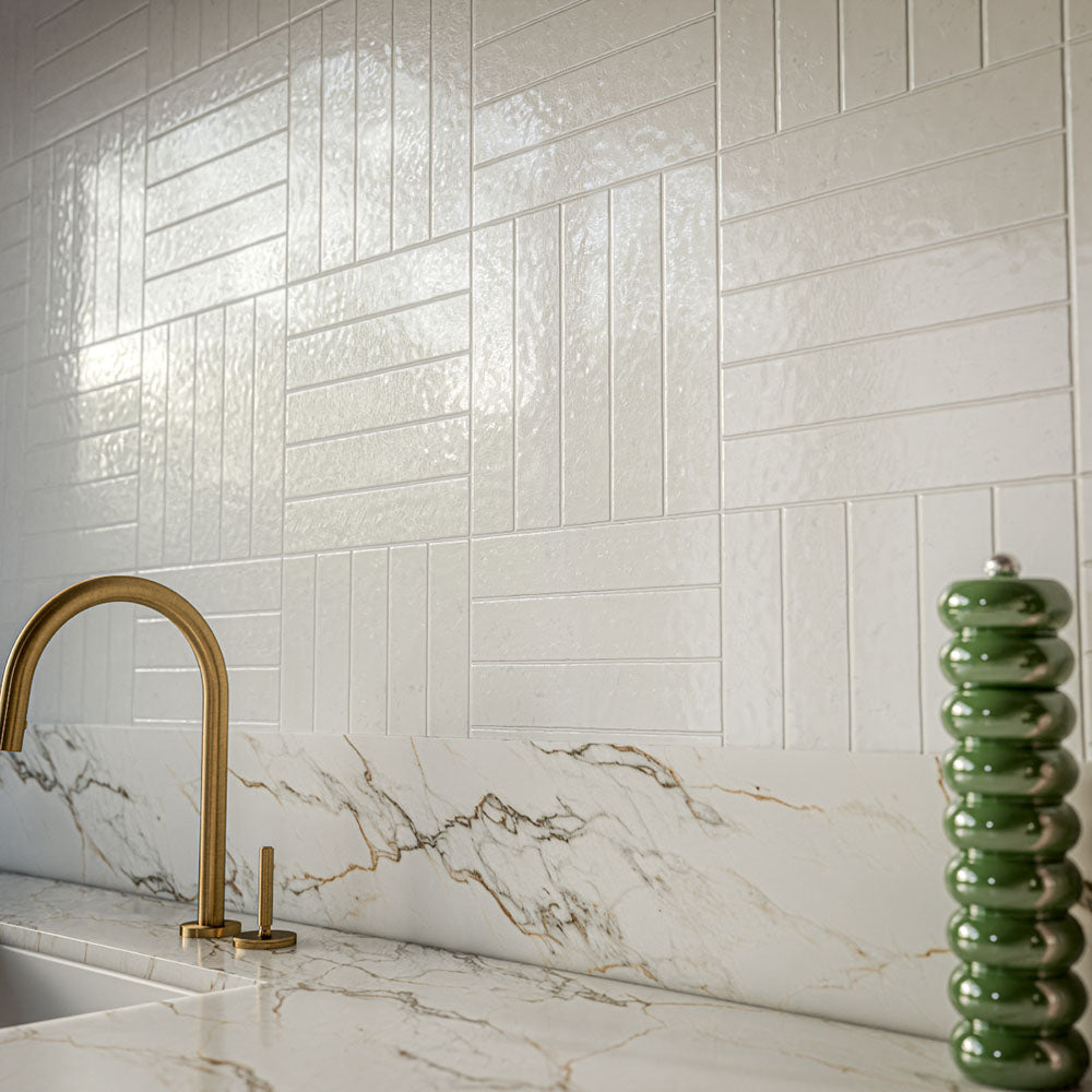 Close-up of Bora Bora White Sand Brick 6.5x32.8cm kitchen wall tiles with a textured flux glaze finish, arranged in a basketweave pattern above marble-effect worktops and a brass tap.