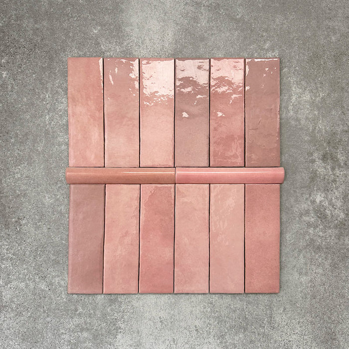 Flat lay showing Zellige Rose Pink Brick 6.5 × 20cm Moroccan-style ceramic tiles paired with a matching Rose Pink Bullnose 3 × 20cm trim tile, displayed in soft blush and dusty pink tones with natural glaze variation and gently uneven edges, arranged on a textured grey background to illustrate the coordinating brick tile and rounded-edge bullnose detail for a handcrafted zellige-effect finish.