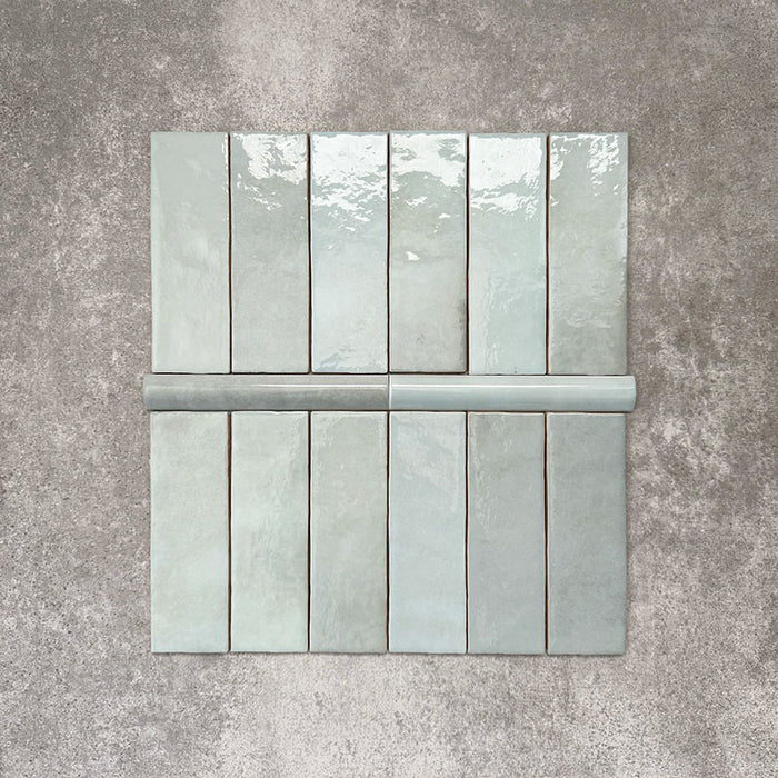 Flat lay of Zellige Aqua Moroccan-style ceramic tiles, showing 6.5×20cm brick tiles paired with a 3×20cm bullnose trim, highlighting the rounded edge detail, glossy blue-green glaze and natural tonal variation on a neutral background.