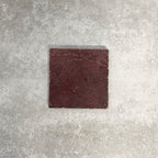 Single Fayrouz Burgundy Red 15.2x15.2cm natural marble tile with a tumbled finish, featuring deep red tones and natural veining, displayed against a textured neutral background in a clean product setting.