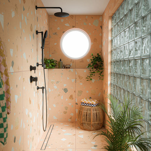 Walk-in shower featuring Byblos Cotto 60cm x 120cm terrazzo effect porcelain wall and floor tiles, with warm terracotta tones, black shower fittings, glass block wall and natural greenery.
