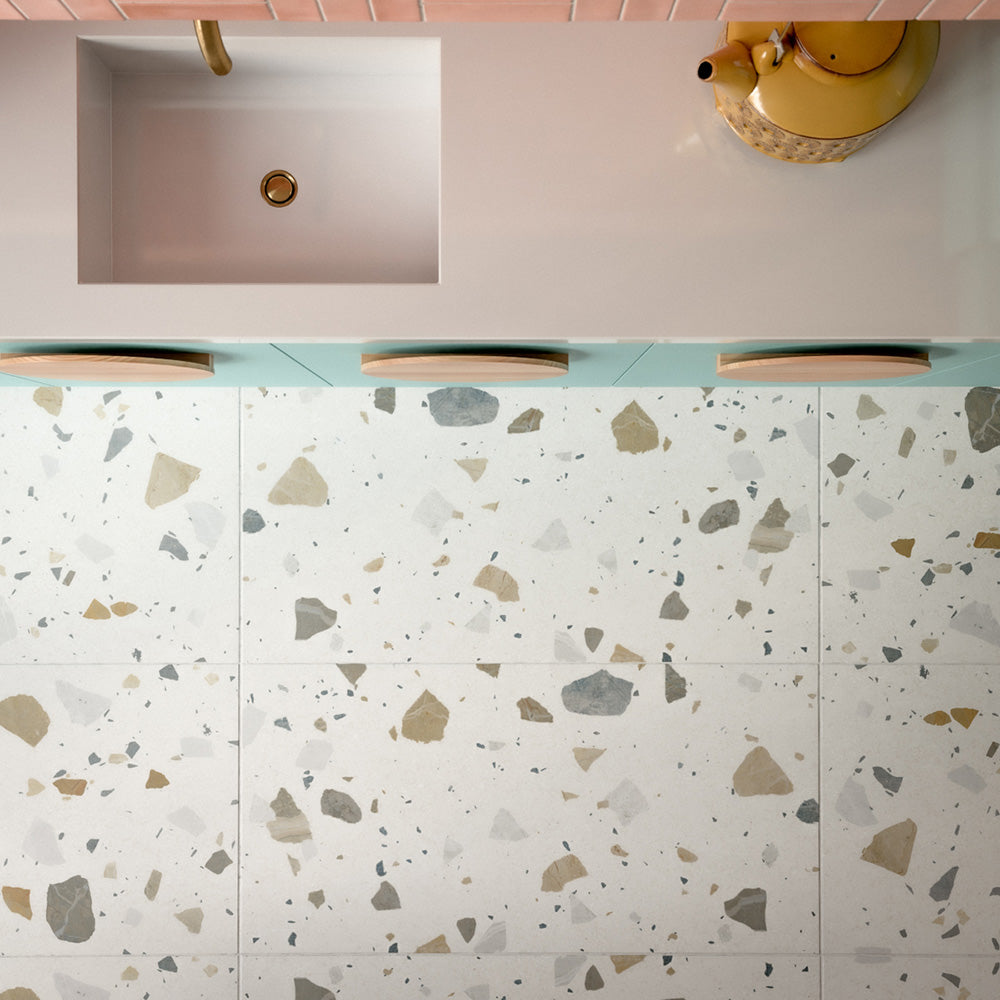 Kitchen featuring Byblos Cotton 60x120cm terrazzo-effect porcelain floor tiles, paired with blush pink Moroccan-style wall tiles, pastel blue cabinetry, and brass fixtures for a playful contemporary interior.