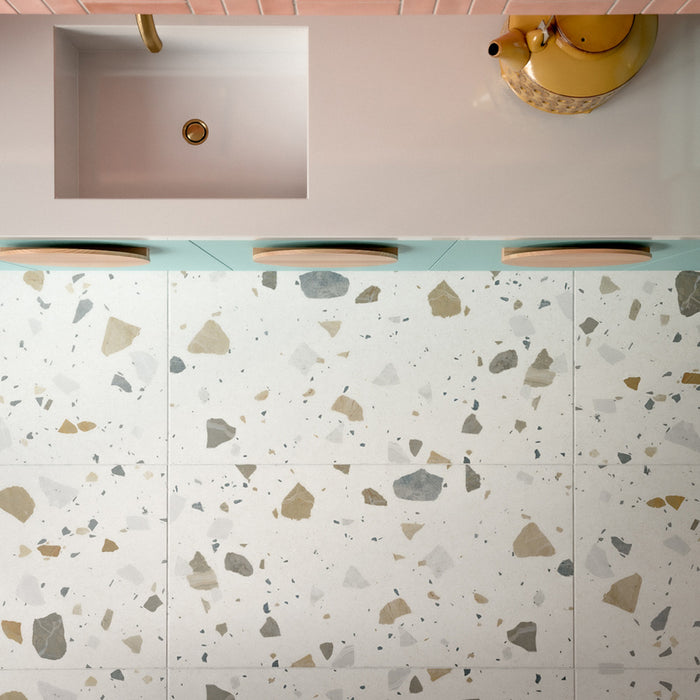 Kitchen featuring Byblos Cotton 60x120cm terrazzo-effect porcelain floor tiles, paired with blush pink Moroccan-style wall tiles, pastel blue cabinetry, and brass fixtures for a playful contemporary interior.