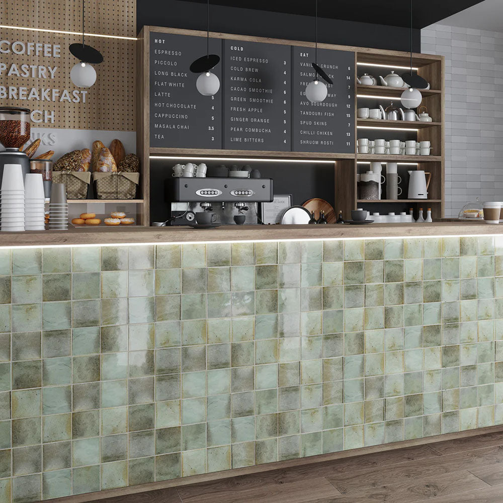 Commercial café counter clad in Saigon Celadon Green Square Wall tiles in a Moroccan-inspired style, featuring 10 × 10cm glossy ceramic tiles in soft green and blue-grey tones with natural colour variation.