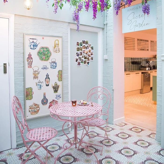 Café interior featuring Cuba La Calle Moroccan-style porcelain floor tiles in a 20×20cm square format, laid in a repeating circular mosaic-style pattern with soft white, terracotta, burgundy and green tones, paired with pastel seating and light-filled interiors to create a charming, decorative finish.