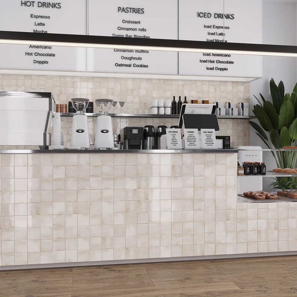 Commercial café counter clad in Saigon White Square Wall tiles in a Moroccan-inspired style, featuring 10 × 10cm glossy ceramic tiles in soft white tones with subtle tonal variation.