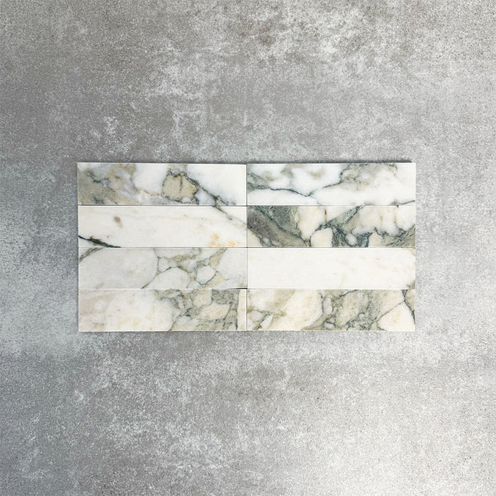 Arrangement featuring Fayrouz Calacatta Green 5x20cm natural marble tiles with a honed finish, displayed in a horizontal layout to showcase soft white tones with green and gold veining against a neutral background.