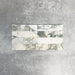 Arrangement featuring Fayrouz Calacatta Green 5x20cm natural marble tiles with a honed finish, displayed in a horizontal layout to showcase soft white tones with green and gold veining against a neutral background.