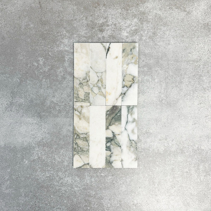 Arrangement featuring Fayrouz Calacatta Green 5x20cm natural marble tiles with a honed finish, displayed in a vertical layout to showcase soft white tones with green and gold veining against a neutral background.