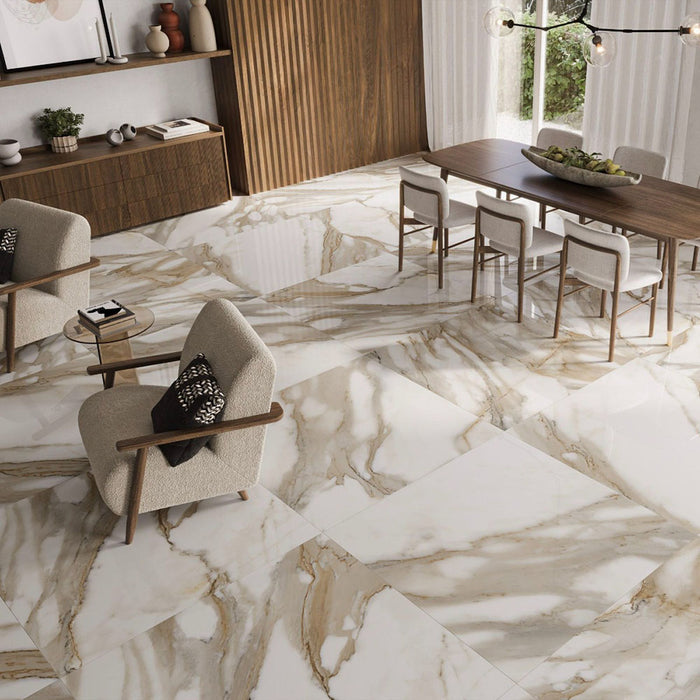 Dining and living space featuring Calacatta Oro Complement 60 × 60cm porcelain floor tiles, showcasing flowing gold veining across a polished surface, paired with warm wood furniture and soft neutral tones for an elegant, contemporary setting.