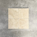 Four Fayrouz Latte Foam 15.2x15.2cm natural marble tiles with a tumbled finish arranged together, showcasing soft cream tones, gentle veining and natural variation against a neutral textured background.