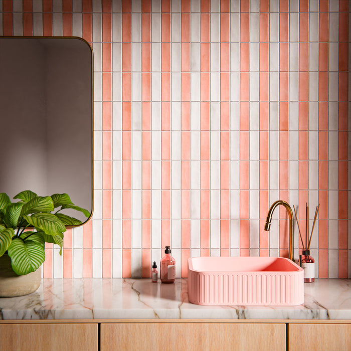 Bathroom vanity area featuring Benomar Moroccan-style brick tiles in soft blush and ivory tones, installed vertically as a statement wall, styled with a fluted pink basin, brushed brass tap, marble surface, and greenery.
