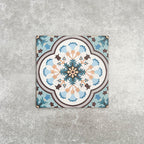 Cuba Bayamo Moroccan style patterned tile in a 20cm x 20cm format, featuring an ornate geometric floral design in soft blue, cream, teal and warm brown tones, displayed against a textured concrete-effect background.