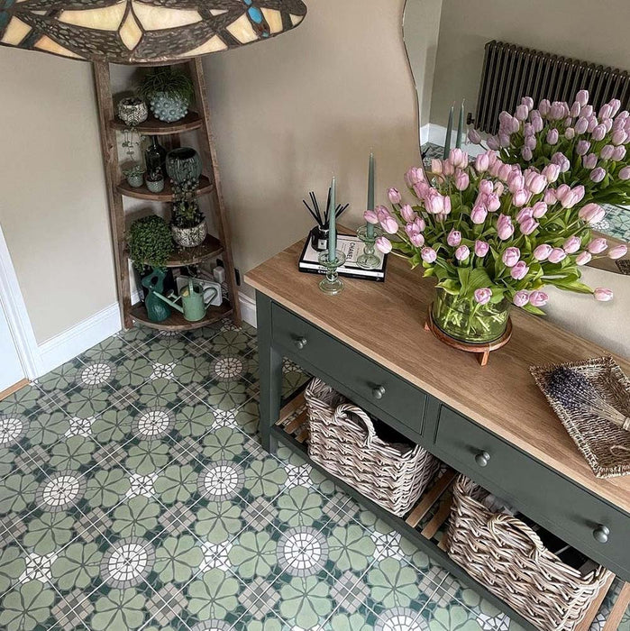Hallway interior featuring Nantes Green Moroccan-style tiles in a 20x20cm format, laid as a decorative patterned floor. The soft green and white floral-inspired design adds a classic, timeless feel, paired with natural wood furniture, woven baskets and fresh flowers to create a warm, welcoming entrance space.