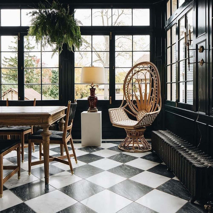 Dining room featuring Florence Grand Calacatta White 50x50cm marble-effect porcelain floor tiles laid in a classic black and white checkerboard pattern, styled with dark painted walls, natural wood furniture and rattan seating for an elegant, characterful interior.