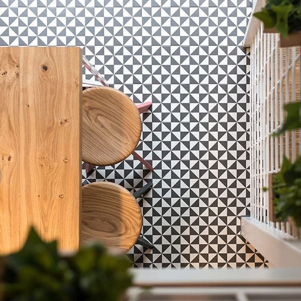Dining area featuring Fulham Tile Black & White Victorian-style porcelain floor tiles in a 25 × 25cm format, laid in a repeating geometric pattern and styled with natural wood furniture and soft greenery for a modern take on a classic black and white floor.
