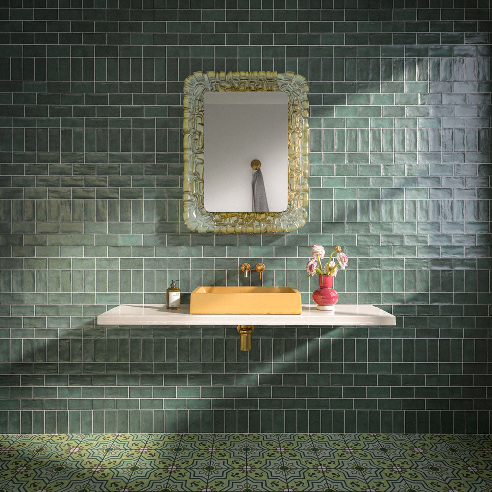 Bathroom featuring Dordogne Green Pines 7.5x15cm rustic gloss wall tiles, showcasing rich green tones with handmade-style shade variation, paired with a white floating vanity, mustard yellow basin, brass fittings, ornate mirror and patterned green floor tiles.