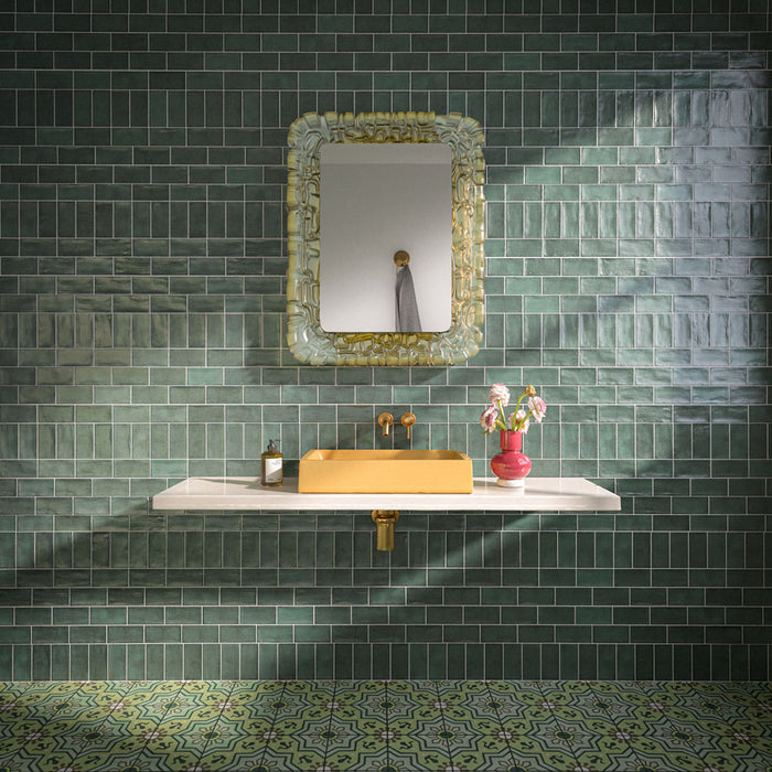Bathroom featuring Dordogne Green Pines 7.5x15cm rustic gloss wall tiles, showcasing rich green tones with handmade-style shade variation, paired with a white floating vanity, mustard yellow basin, brass fittings, ornate mirror and patterned green floor tiles.