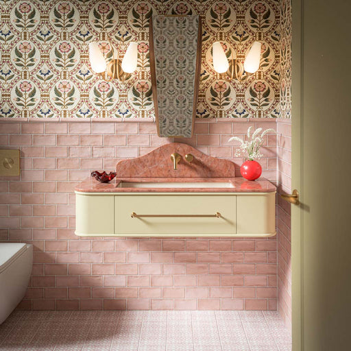 Dordogne Pink Dust 7.5cm x 15cm rustic effect gloss wall tiles, creating a soft pink bathroom scheme with subtle shade variation, paired with floral patterned walls, warm cream cabinetry and brass details.