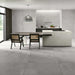 Kitchen interior featuring Etna Grey Matt 30 × 60cm porcelain floor tiles, styled with a modern island, dark cabinetry, woven dining chairs, and soft grey tones for a sleek, contemporary finish.