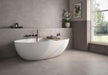Bathroom interior featuring Etna Grey Matt 60 × 60cm porcelain wall and floor tiles, styled with a freestanding bath, black fittings, soft neutral tones, and natural light for a calm, contemporary space.