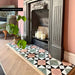 Living room featuring Farnham Manor 20x20cm Victorian-style floor tiles, styled as a decorative fireplace hearth with soft pink walls, herringbone wood flooring, period features and botanical accents.