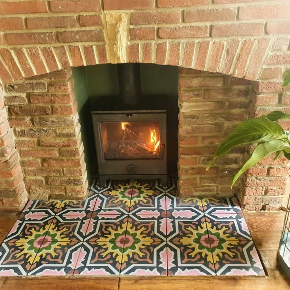 Fireplace hearth featuring Cuba Havana Moroccan-style porcelain tiles in a 20×20cm square format, showcasing a bold geometric pattern in navy, pink, green and mustard tones, framed by exposed brickwork and a wood-burning stove for a warm, character-filled finish.