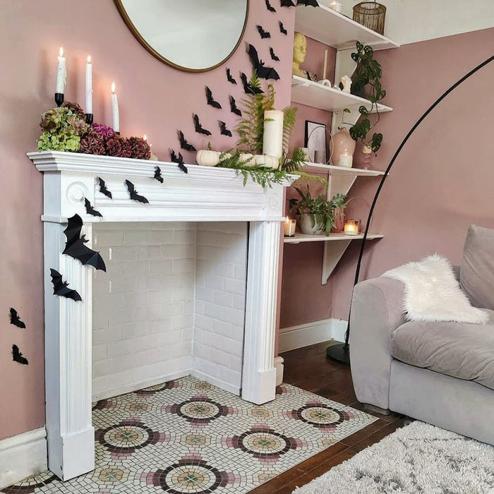 Living room fireplace hearth featuring Cuba La Calle Moroccan-style porcelain tiles in a 20×20cm square format, laid in a repeating circular mosaic-style pattern with soft white, terracotta, burgundy and green tones, framed by a white mantel and blush pink walls to create a decorative focal point.
