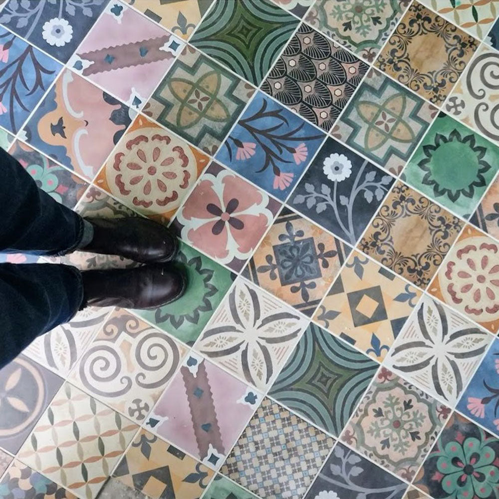 Interior floor featuring Cuba Patchwork Moroccan-style porcelain tiles in a 20×20cm square format, laid in a mixed patchwork arrangement combining geometric, floral and traditional motifs in earthy, green, blue and terracotta tones, shown from above to highlight the variety of patterns and colours.