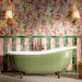 Bathroom featuring Foundry Coral Pink 6.5x20cm gloss wall tiles, arranged vertically alongside jade green tiles, paired with colourful floral wallpaper, a freestanding sage green bathtub, brass fixtures and terrazzo effect floor tiles.