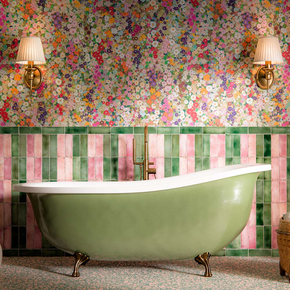 Bathroom featuring Foundry Jade Green 6.5x20cm gloss wall tiles, arranged vertically alongside soft pink tiles, paired with colourful floral wallpaper, a freestanding sage green bathtub, brass fixtures and terrazzo effect floor tiles.